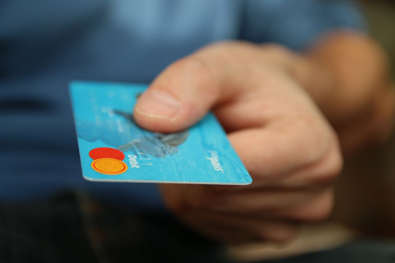 About A close-up shot of a hand offering a blue debit card for payment.