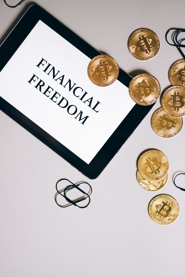 About Top view of a tablet displaying 'Financial Freedom' with Bitcoin coins scattered around.